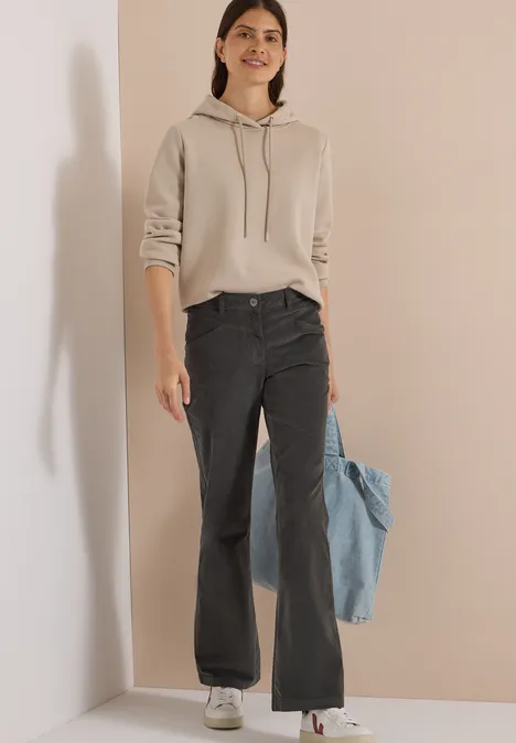 Femme en sweat beige, jean noir ample, tenant une veste en jean bleue.