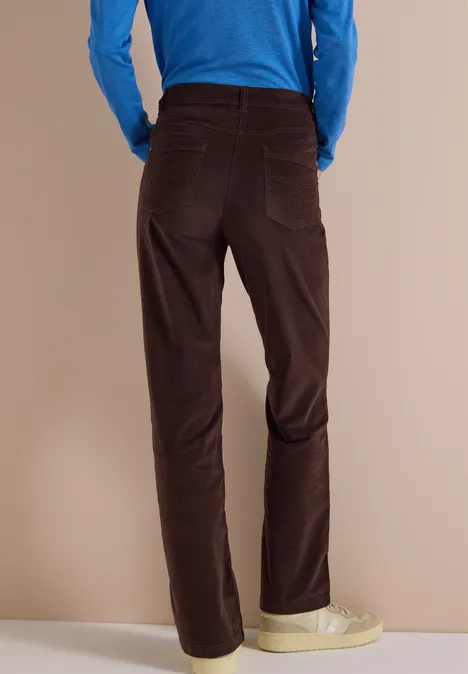 High Waist Bootcut Hose im Slim Fit truffle brown Rückansicht einer Person mit dunkelbraunen Cordhose, blauem Oberteil und hellen Sneakers vor neutralem Hintergrund.