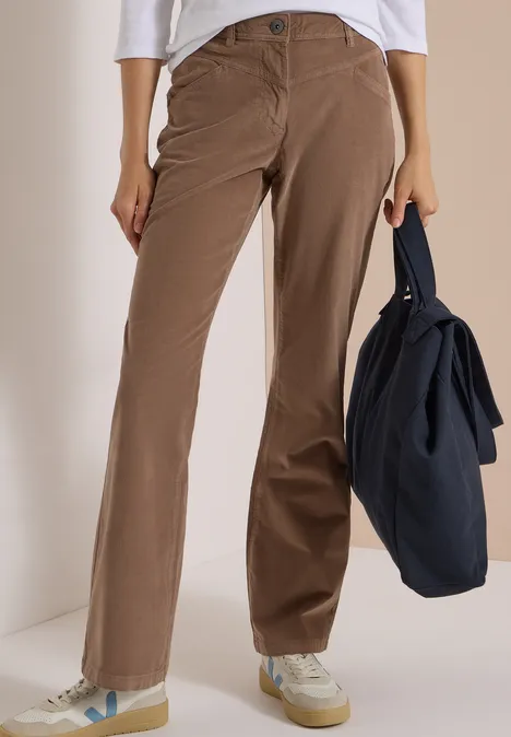 Une personne porte un pantalon en velours côtelé marron et des baskets blanches, tenant un sac bleu foncé.