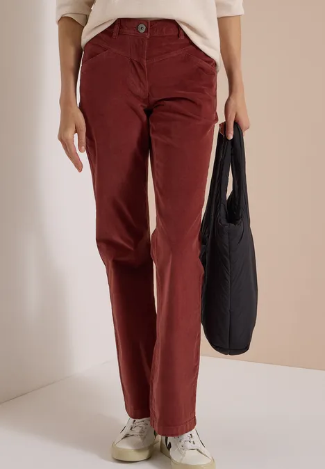 Une personne porte un pantalon en velours côtelé bordeaux, des baskets blanches et tient un sac noir.
