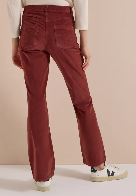 Pantalon en velours côtelé rouge à coupe ample, poches arrière, porté avec des baskets blanches sur fond neutre.