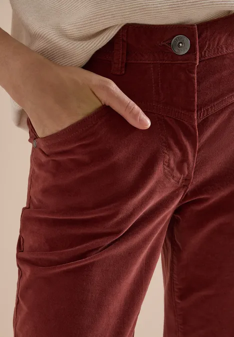 Gros plan sur un pantalon en velours côtelé rouge-brun avec une main dans la poche.