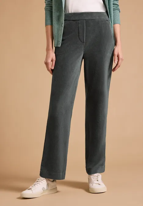High Waist Straight Leg Hose w kroju Loose Fit easy khaki Kobieta w ciemnoszarych spodniach sztruksowych o prostym kroju, z bocznymi kieszeniami i białych trampkach.