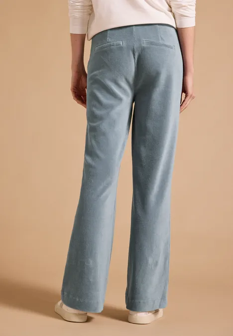 Spodnie z wysokim stanem i prostymi nogawkami w kroju Loose Fit dove blue Kobieta widziana od tyłu w jasnoniebieskich, szerokich dżinsach na beżowym tle.