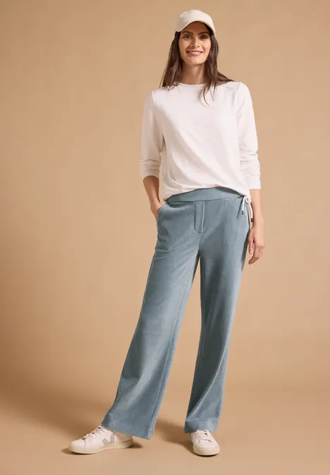 Spodnie z wysokim stanem i prostymi nogawkami w kroju Loose Fit dove blue Kobieta w białej czapce, białej bluzce i luźnych niebieskich spodniach, uśmiecha się na beżowym tle.