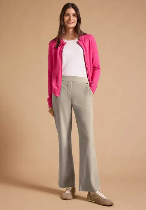 Spodnie z wysokim stanem i prostymi Straight Leg nogawkami o Loose Fit kroju silvery beige Kobieta w różowym kardiganie, białym t-shircie, szarych dzwonach i trampkach na neutralnym tle.