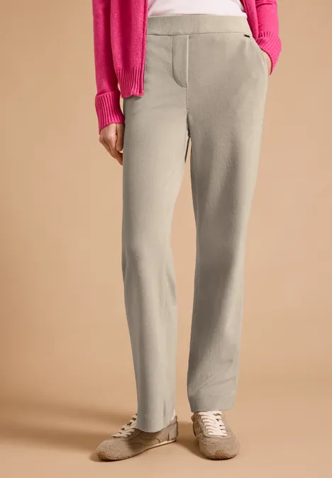 Spodnie z wysokim stanem i prostymi Straight Leg nogawkami o Loose Fit kroju silvery beige Beżowe spodnie dresowe z kieszeniami i jasne buty sportowe, różowy sweter na neutralnym tle.