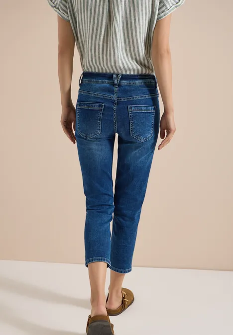 Rückansicht einer Person in gestreiftem Top und knöchellangen, blauen Jeans vor neutralem Hintergrund.