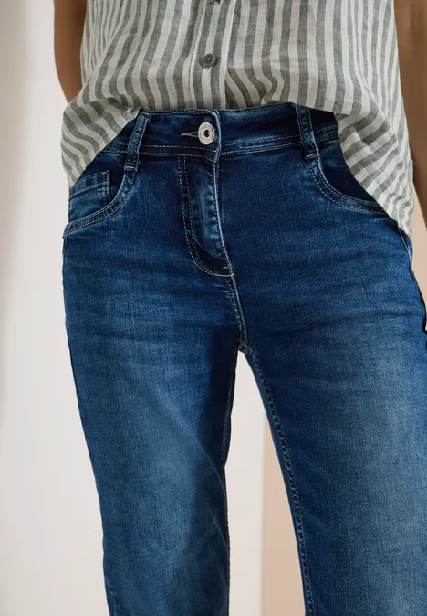 Eine Person trägt blaue Jeans und ein gestreiftes Hemd, Hände in den Hosentaschen.