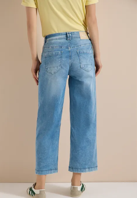 Rückansicht einer Person in weit geschnittenen, hellblauen, knöchellangen Jeans und gelbem T-Shirt.