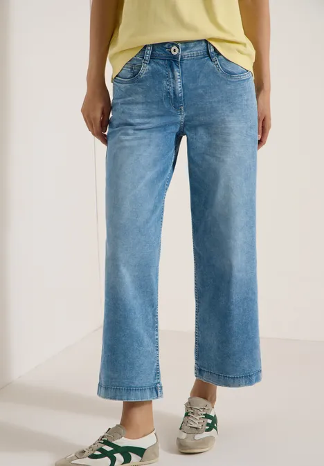 Eine Person trägt weite, kürzere Hellblaue Jeans und Sneakers vor weißem Hintergrund.