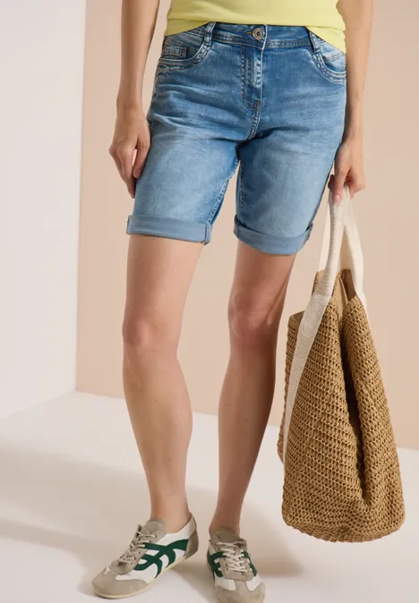 Short taille haute Slim Leg, coupe ajustée authentic used wash Vue sur jambes: femme en bermuda en jean, baskets décontractées et sac de plage en paille.