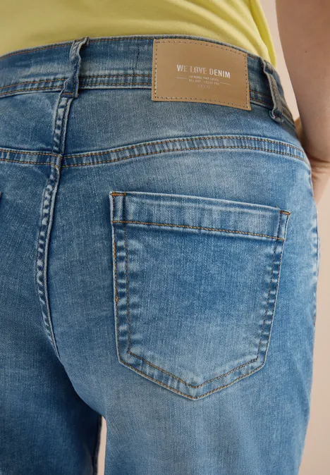 Short taille haute Slim Leg, coupe ajustée authentic used wash Vue arrière d'une personne en jean bleu avec poche arrière et étiquette de marque, haut jaune visible.