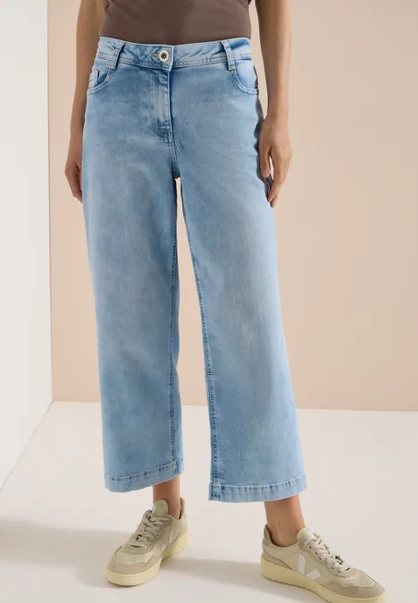7/8 High Waist Jeans im Loose Fit light blue random bleached Frau trägt helle, weite 7/8-Jeans und beigefarbene Sneaker.