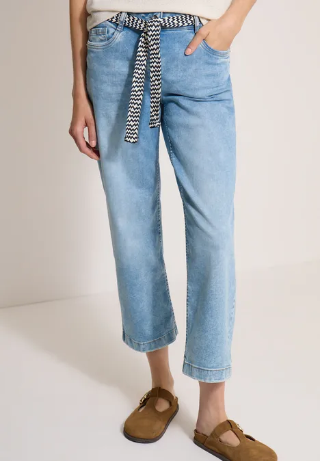 Jean bleu clair décontracté à ceinture zébrée, coupe cheville, porté avec des mocassins marron.