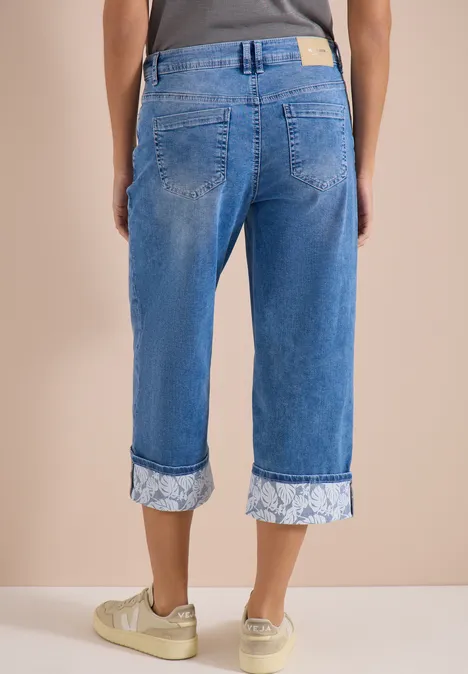 7/8 Wide Leg Jeans mit Turn-Up-Detail mid blue wash Rückansicht: Person trägt hellblaue, umgeschlagene Capri-Jeans mit floralem Muster und weiße Sneaker mit Goldakzenten.