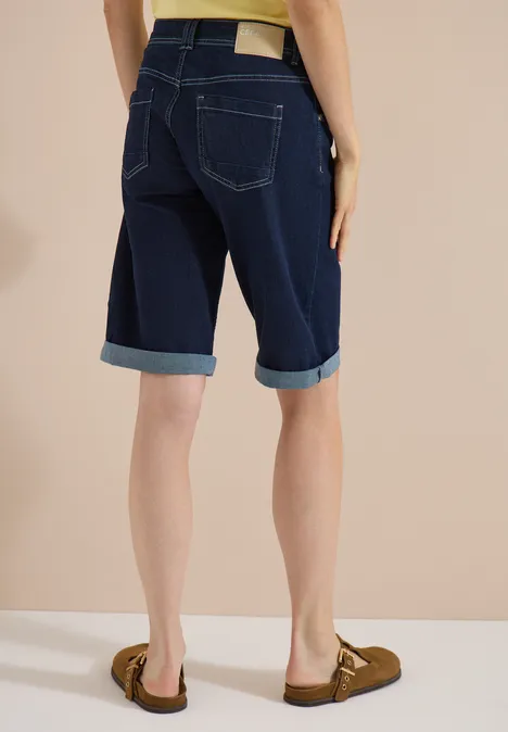 Vrouw van achteren in een donker gewassen omgeslagen denim Bermuda-short met bruine loafers.