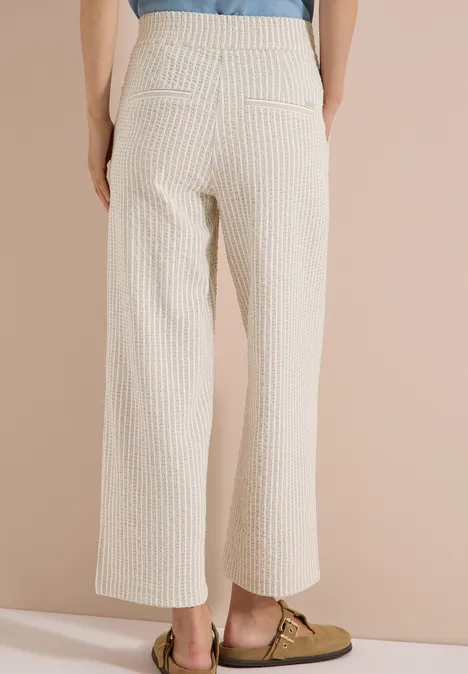 Pantalon large en qualité seersucker grain beige Vue arrière d'une personne portant un pantalon blanc à fines rayures et des mocassins bruns.