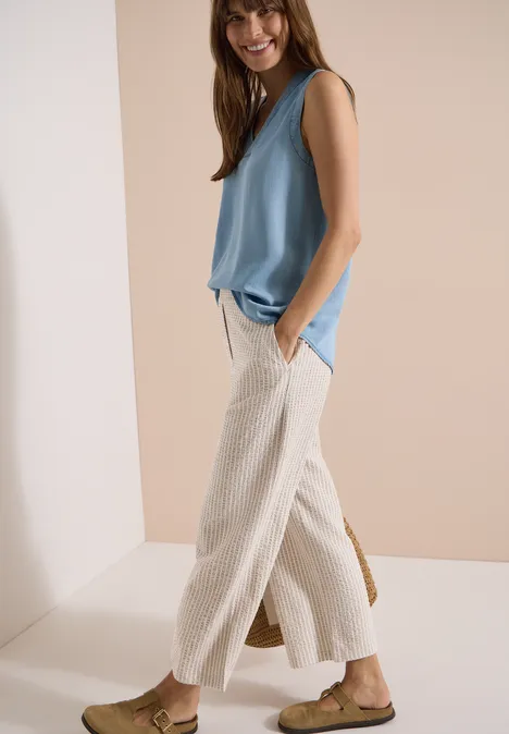 Pantalon large en qualité seersucker grain beige Mannequin en haut sans manches bleu clair, pantalon ample crème et sandales plates.