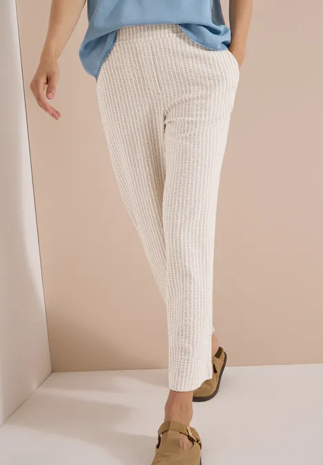 Pantalon large en qualité seersucker grain beige Jambes en pantalon côtelé beige clair, longueur cheville, portées avec des mocassins sur fond neutre