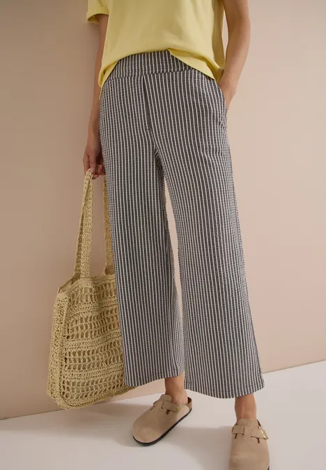 Femme en pantalon ample rayé gris, haut jaune, sac en osier et mocassins beiges.