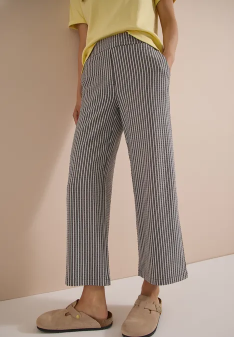 Pantalon ample à rayures verticales et mocassins beiges portés par une personne devant un fond uni