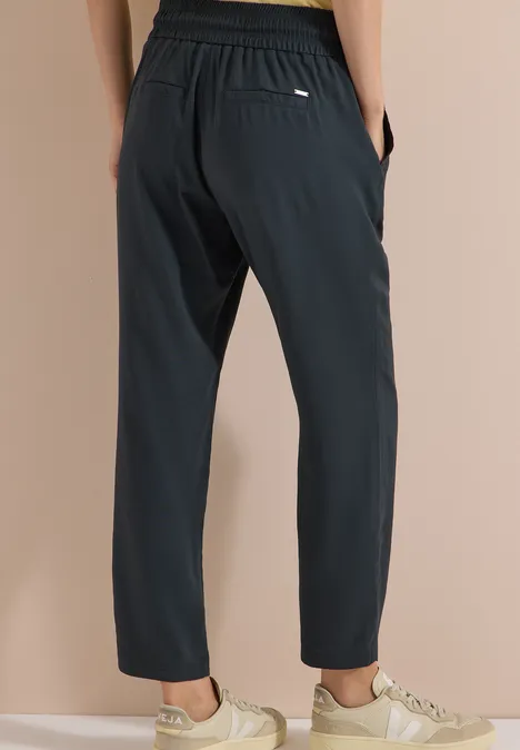 Schwarze, locker sitzende Hose mit Gummibund und Taschen, kombiniert mit hellen Sneakern.