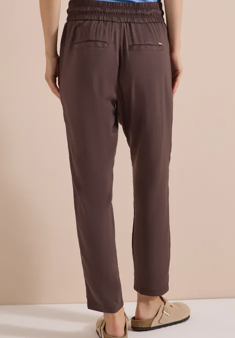Dunkelbraune, hoch taillierte Hose mit elastischem Bund und schmal zulaufenden Beinen, dazu Loafers.