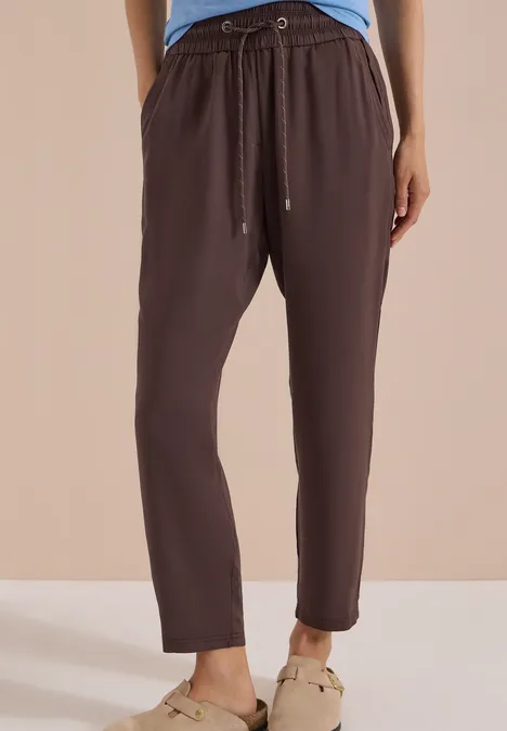 Damenhose aus braunem, leichtem Stoff mit Gummibund und Kordel sowie schmal zulaufenden Beinen.