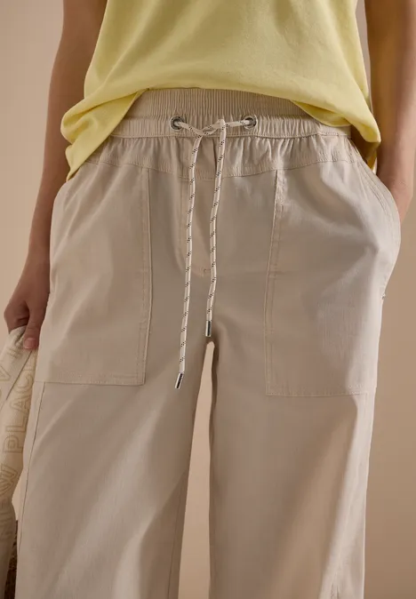 Weit geschnittene hellbeige Hose mit Kordelzugbund und aufgesetzten Taschen, kombiniert mit gelbem Top.