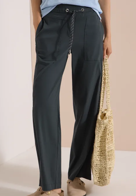 Schlichte schwarze Hose mit Tunnelzug, weiten Beinen und sommerlicher Stroh-Tasche.