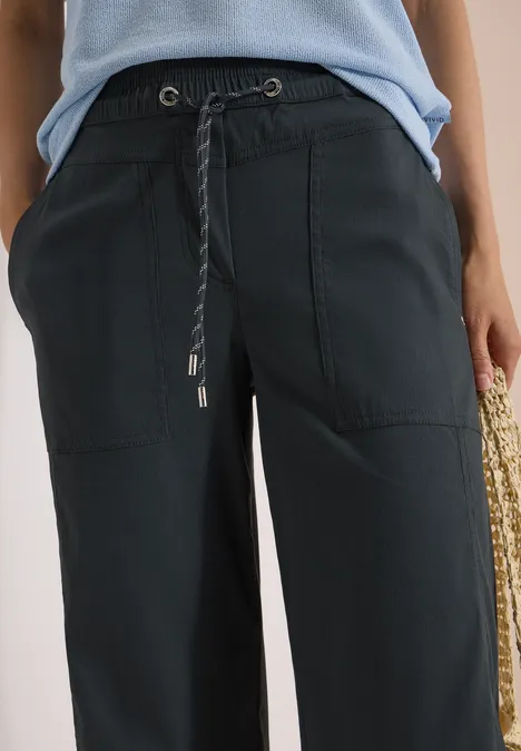 Schwarze, weite Hose mit Kordelzug und aufgesetzten Taschen, kombiniert mit einem hellblauen Top.