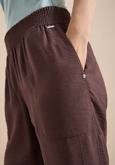 Mid Waist Slim Leg Hose im Loose Fit brown cacao Nahaufnahme von lockeren, braunen Stoffhosen mit elastischem Bund und Taschen.