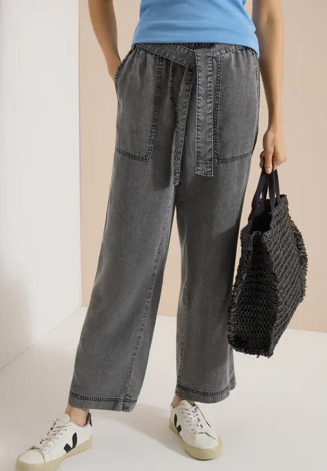 Pantalon à jambes larges avec ceinture à nouer mid grey random wash Femme en jean gris ample à taille nouée, baskets blanches et sac en maille noir.