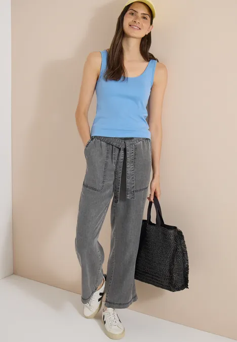 Pantalon à jambes larges avec ceinture à nouer mid grey random wash Femme en débardeur bleu, pantalon ample gris, baskets blanches, portant un grand sac en osier noir.