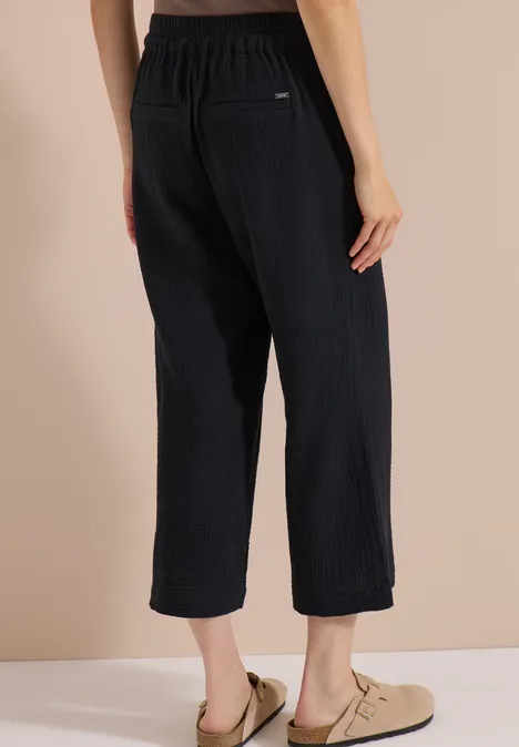 Rückenansicht: schwarze, weite, knöchellange Rippstrick-Hose mit elastischem Bund und hellen Slippers.