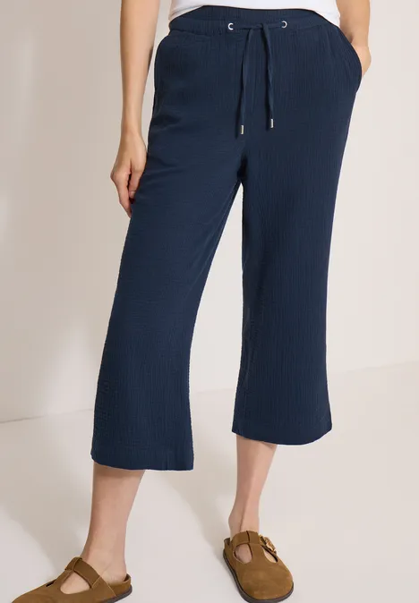 Pantalon 3/4 à jambes larges en mousseline universal blue Un pantalon bleu marine mi-long ample avec cordon et poches, porté avec des chaussures marron.