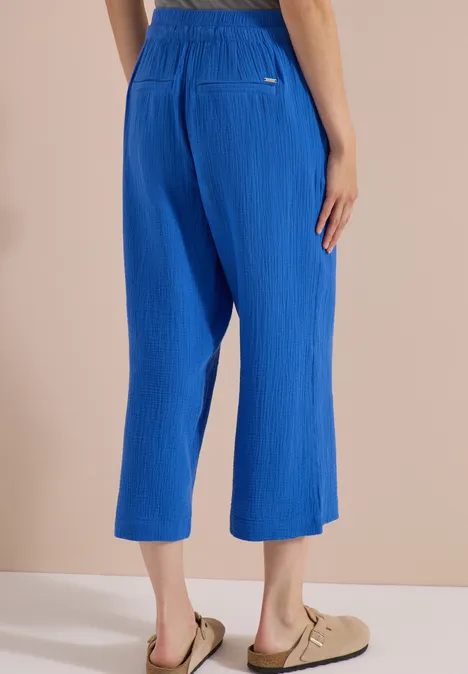 Blaue, plissierte 7/8-Hose mit elastischem Bund, weit geschnitten, kombiniert mit beigen Sandalen.