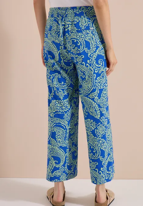 Rückansicht einer Person in weiten Hosen mit blau-grünem Paisley-Muster und flachen Sandalen.