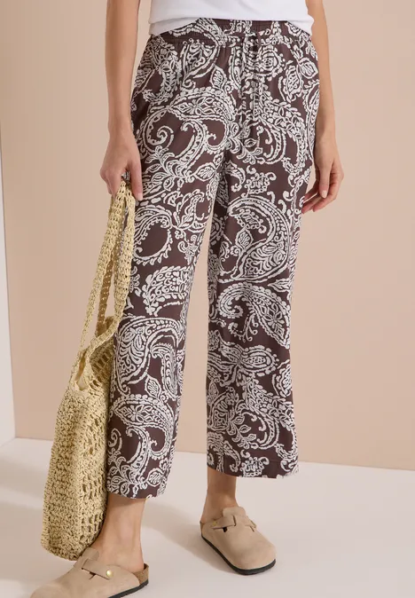 Schwarz-weiße, locker geschnittene Palazzohose mit Paisley-Muster, dazu Basttasche und Loafers.