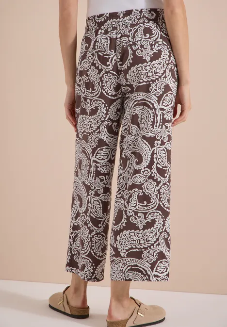 Rückenansicht einer Person in braunen, knöchellangen Culottes mit weißem Paisley-Muster und beige Loafers.