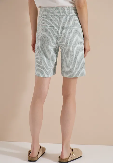 Rückansicht einer Person in hoch taillierten, hellgrün-weiß gestreiften Bermuda-Shorts.