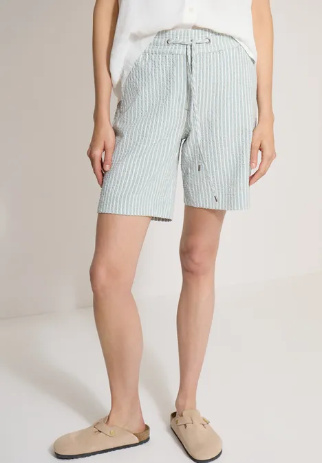 Leichte gestreifte Bermuda-Shorts mit Gürtel, hoher Taille, kombiniert mit weißem Shirt und beigen Slip-ons.