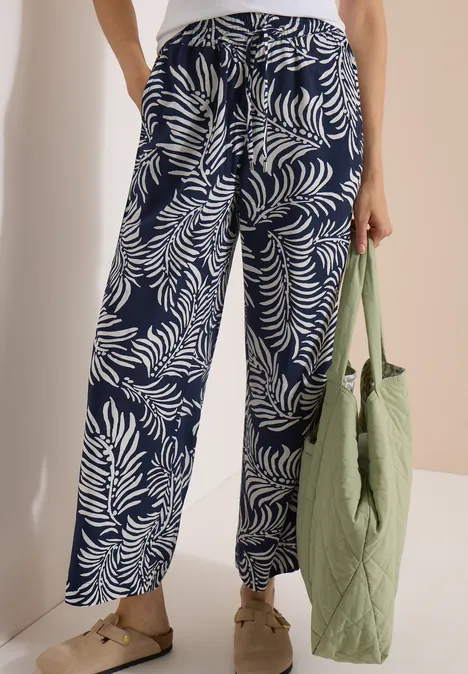 Pantalon à jambes larges avec imprimé et galons universal blue Une personne porte un pantalon large bleu marine à motifs de fougères blanches et tient un sac matelassé vert.