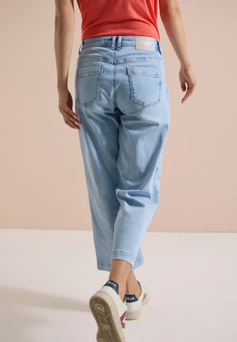 Person in rotem Top und hellblauen Jeans von hinten, mit weißen Sneakern.