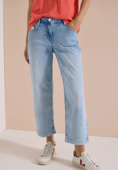 Modische, hellblaue, weit geschnittene Jeans bis zur Knöchelhöhe, kombiniert mit weißen Sneakers.