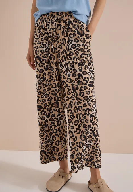 Benen in wijde beige-zwart luipaardprint broek, gecombineerd met beige schoenen en licht topje.