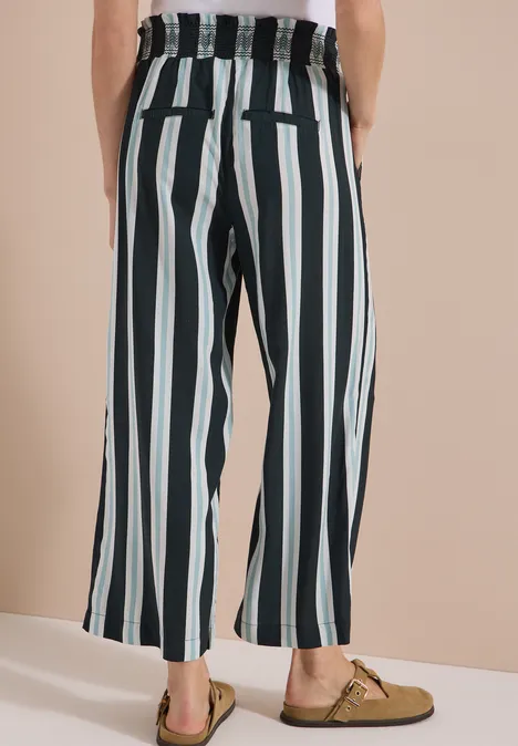 Pantalon taille haute à jambes larges à rayures palm breeze green Personne vue de dos portant un pantalon ample taille haute à fines rayures verticales noires et blanches et des mocassins.
