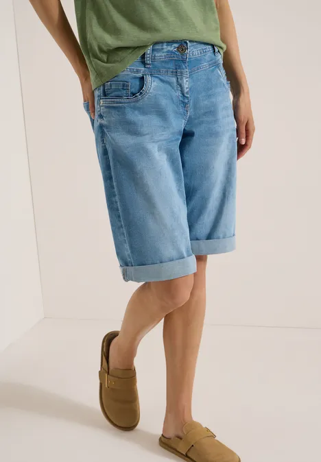 Unterkörper einer Person in hellblauen Jeans-Shorts bis zum Knie und braunen Slippern.