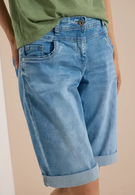 Person trägt grünes T-Shirt und hellblaue Jeans-Bermuda mit umgeschlagenem Saum.